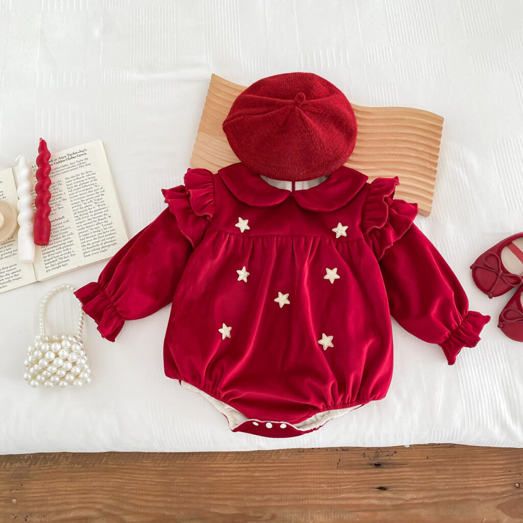 Charming red velvet baby romper embellished with delicate gold star appliqués, exuding a celestial and festive vibe. This outfit features ruffled shoulder details, a Peter Pan collar, and elasticized cuffs for a comfortable yet stylish fit. Styled with a matching red beret, pearl bag, and adorable baby shoes, it’s an ideal choice for holiday celebrations or special occasions.