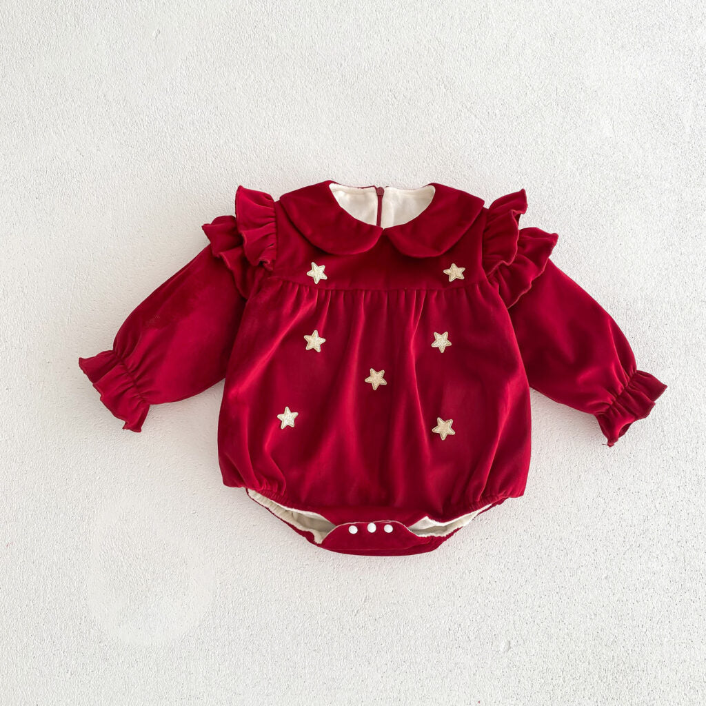 Twinkle Star Velvet Baby Romper laid flat on a white surface. The romper features a deep red velvet texture, a Peter Pan collar, ruffled sleeves, and star appliqué embellishments on the front. It includes elastic cuffs and a convenient snap-button closure at the bottom for easy diaper changes. Simple yet elegant, perfect for festive occasions.