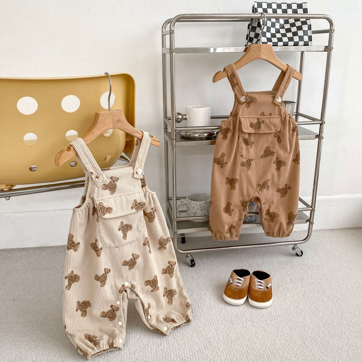 Bear print baby overalls in beige and brown hanging in a nursery