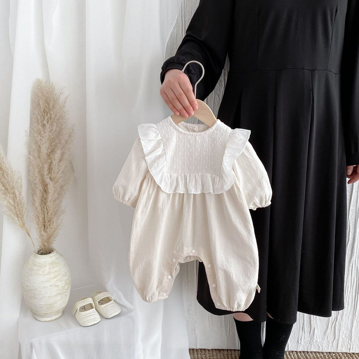 Beige lace collar baby romper held on a hanger