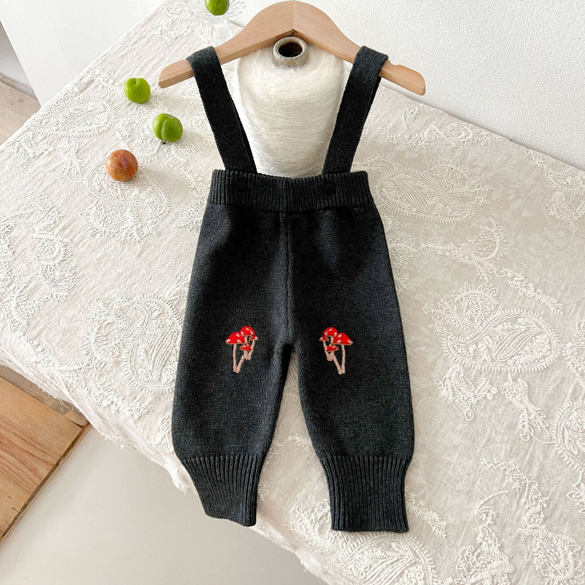 Black knit suspender pants with red mushroom embroidery on a hanger