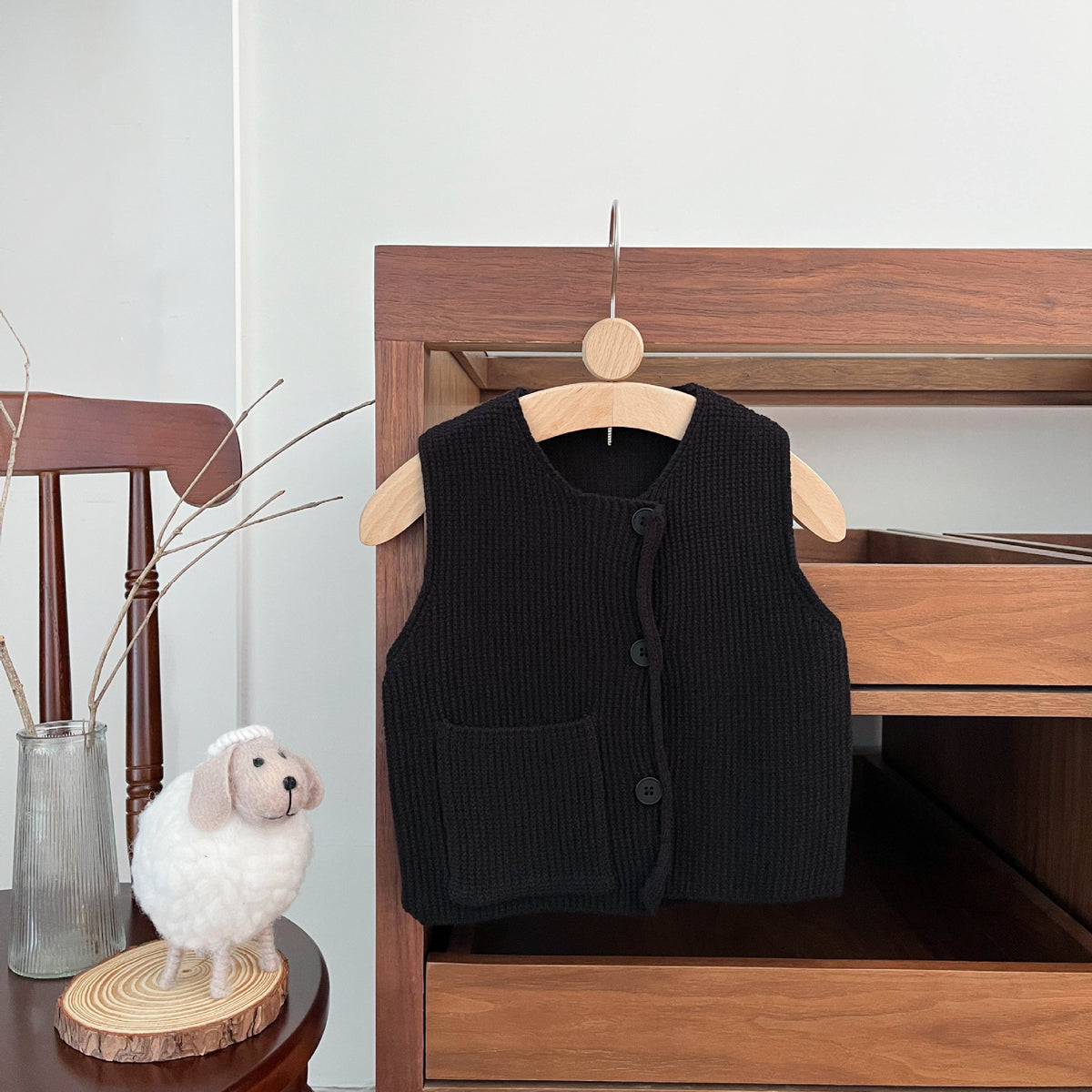 Black knitted toddler vest on a wooden hanger