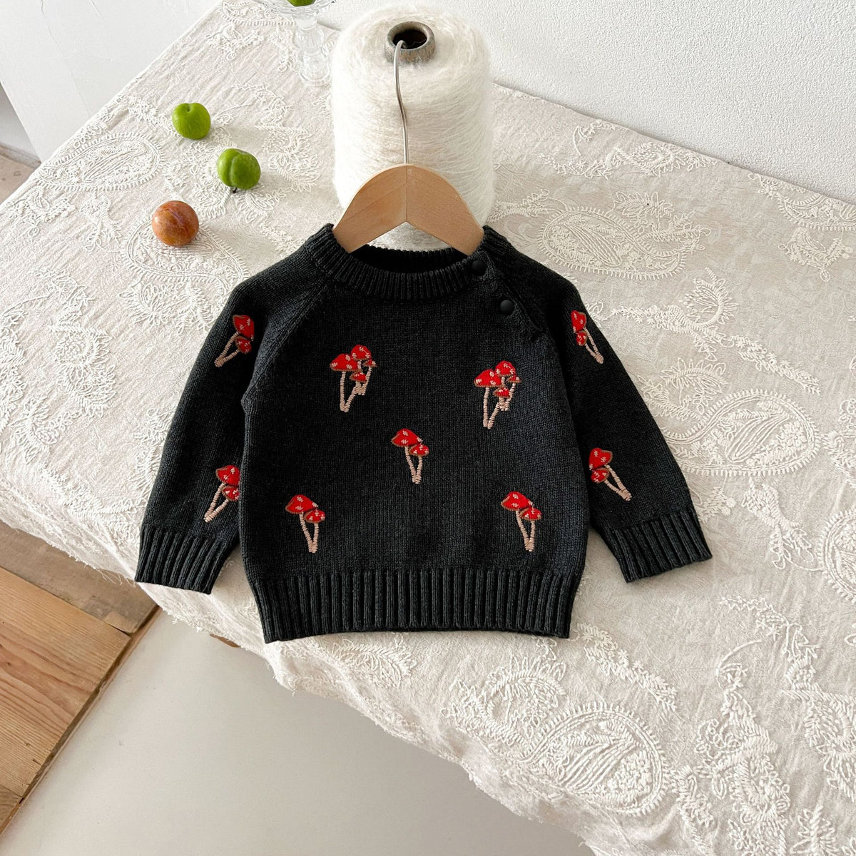 Black knit baby sweater with red mushroom embroidery on a hanger