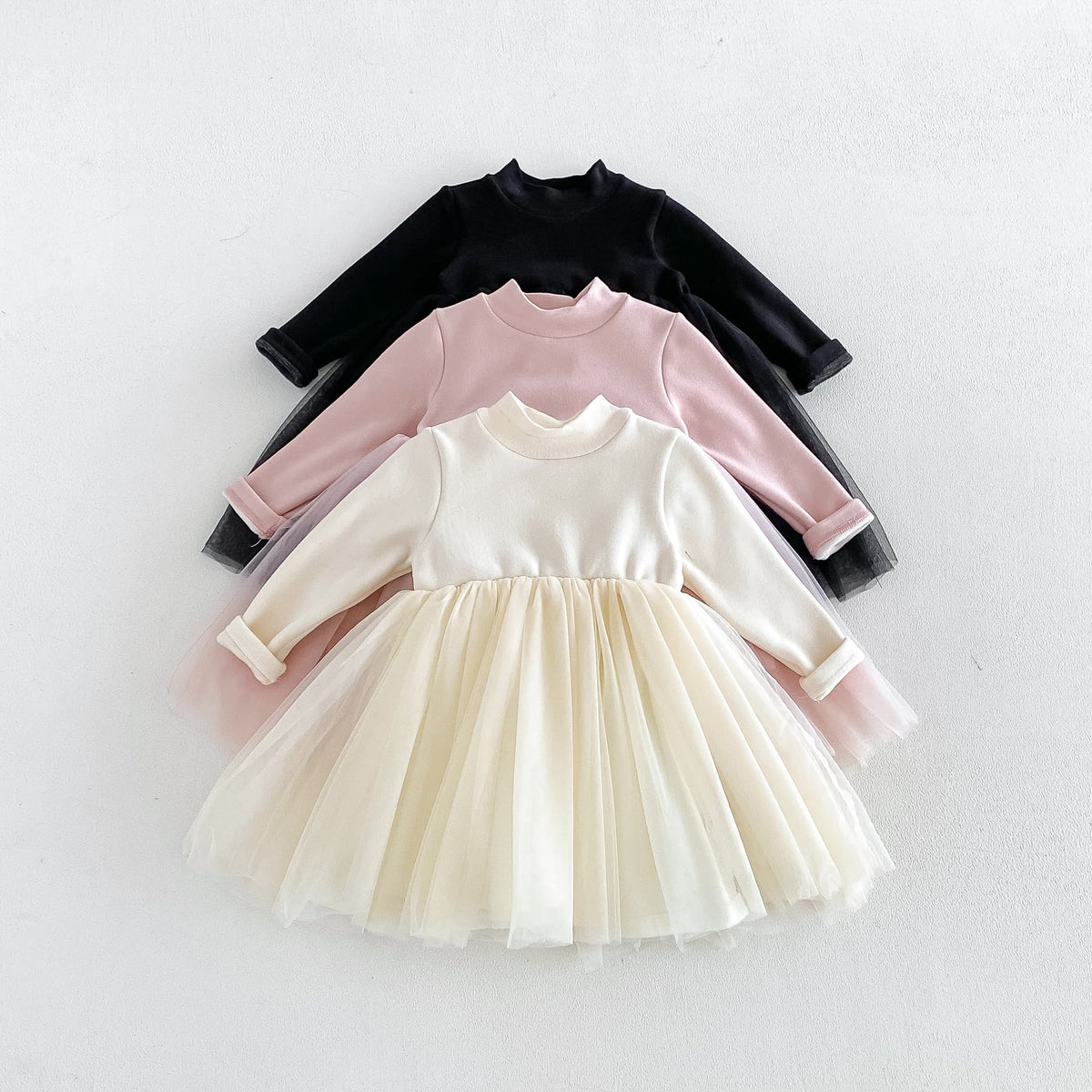 Cream, blush and black long-sleeve tulle dresses for toddler girls, flat lay