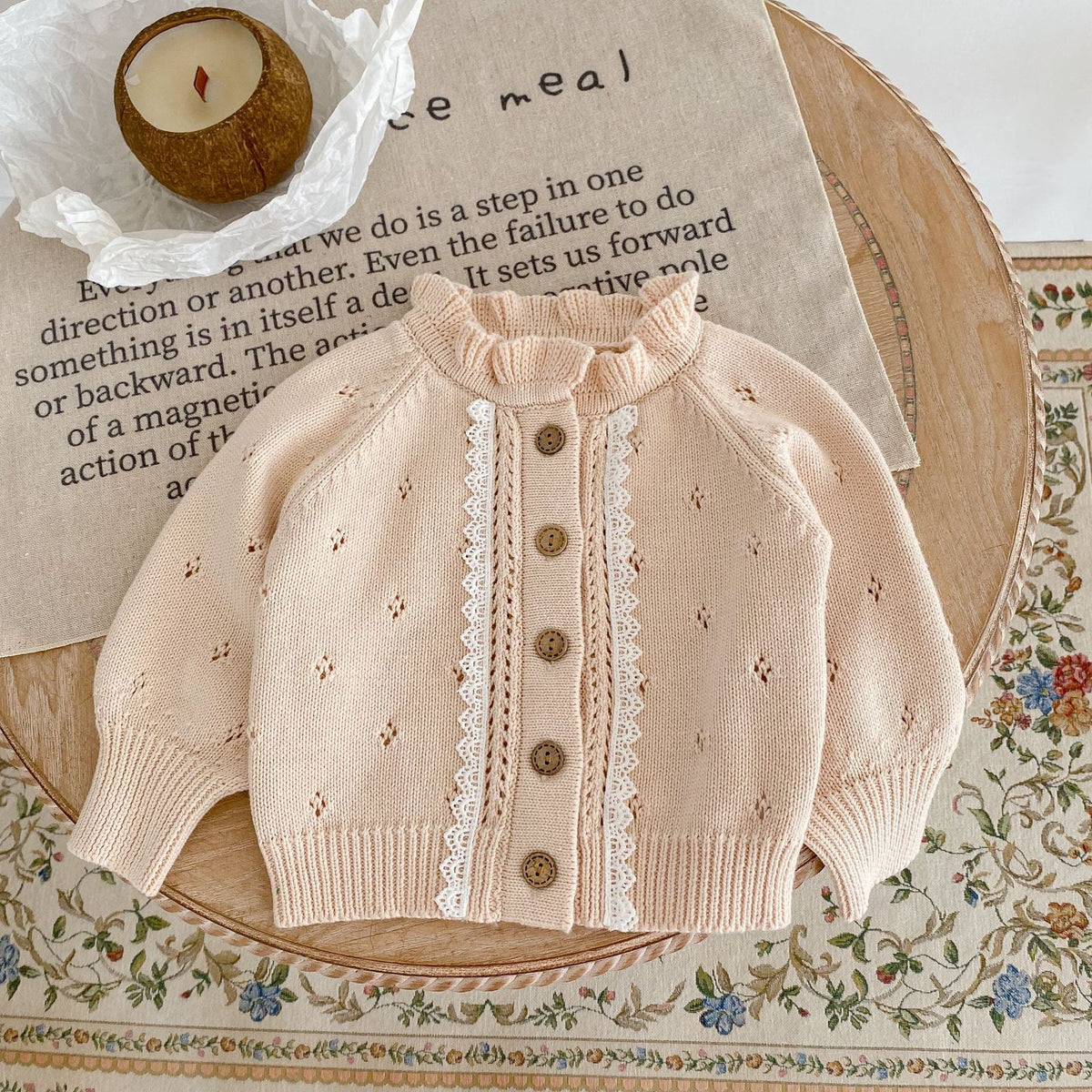 Cream knit baby cardigan with ruffle collar, lace trim and wooden buttons, flat lay