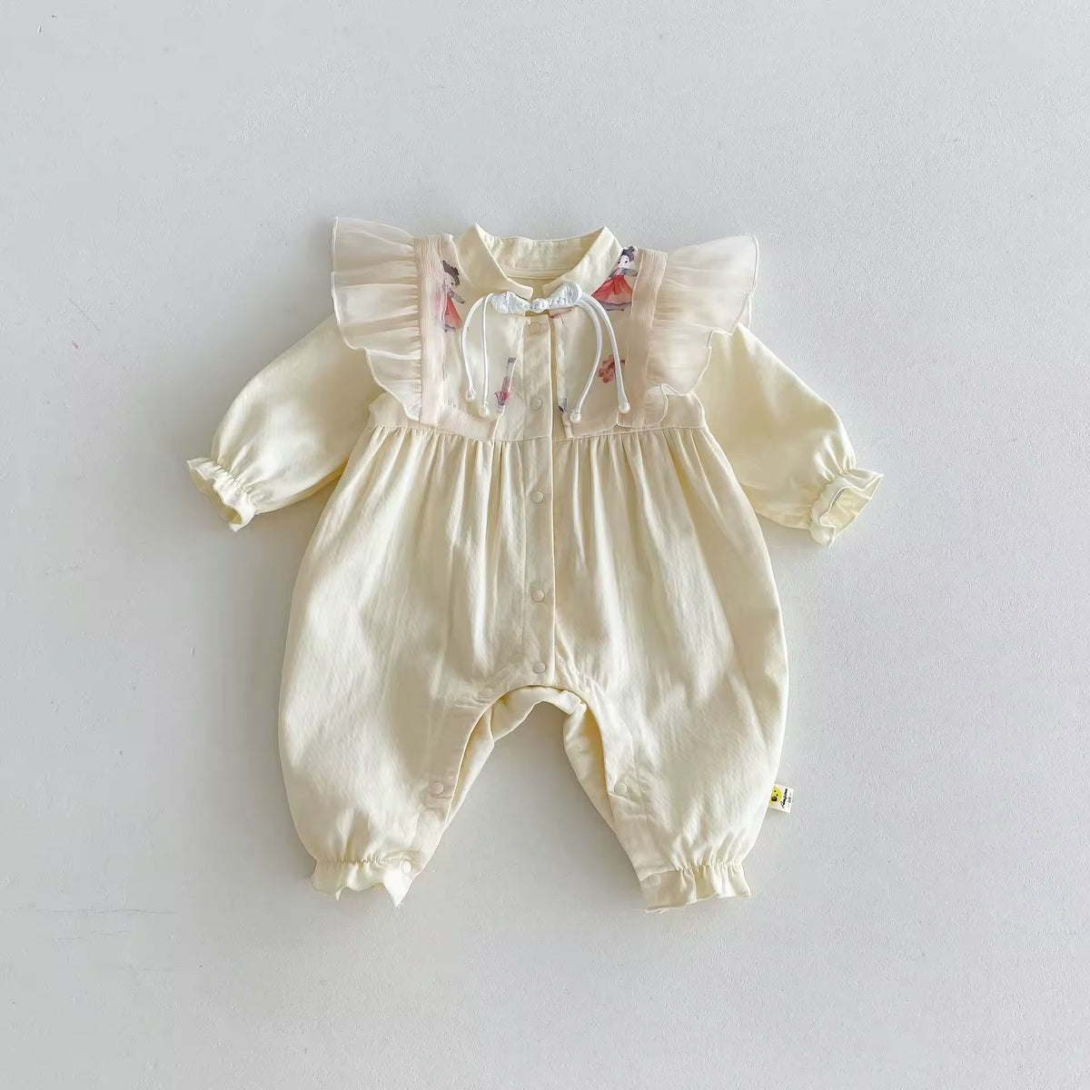 Front view of cream long sleeve baby jumpsuit with ruffle shoulders