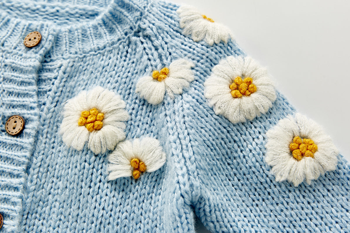 Close-up of 3D daisy flowers on blue knit cardigan