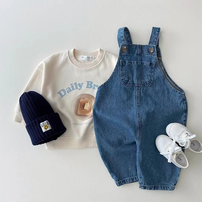 Denim baby overalls styled with cream sweatshirt, navy beanie and sneakers
