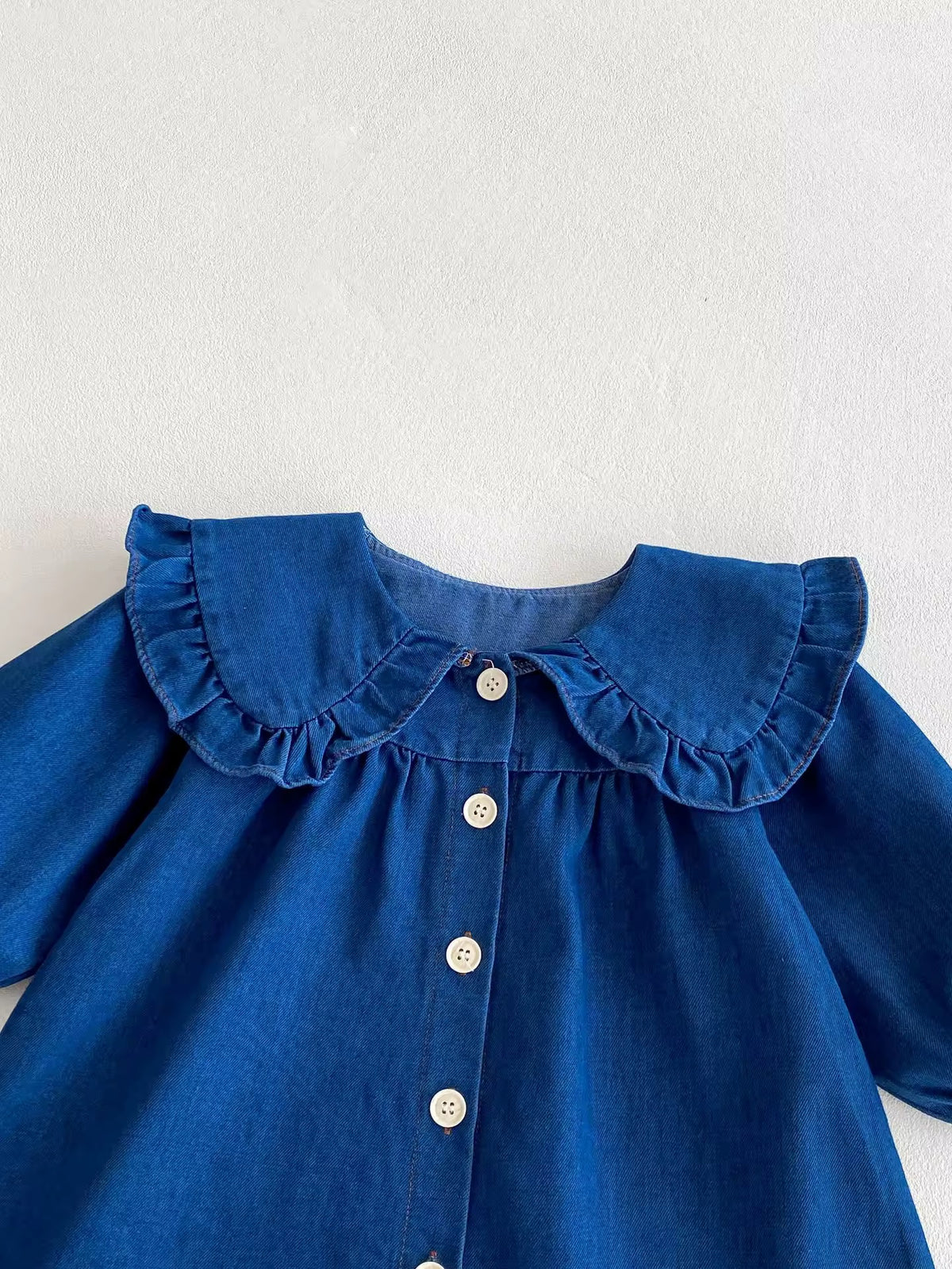 Close-up of ruffle collar and white buttons on denim baby dress