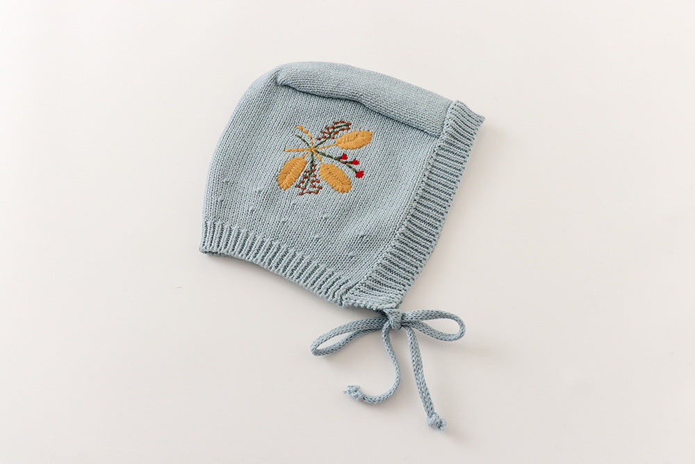 Dusty blue knit baby bonnet with embroidered leaf detail and tie strings