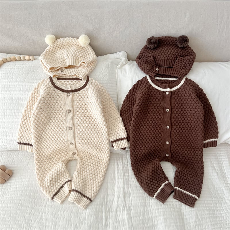 Cream and brown knit bear rompers with hats laid on a bed