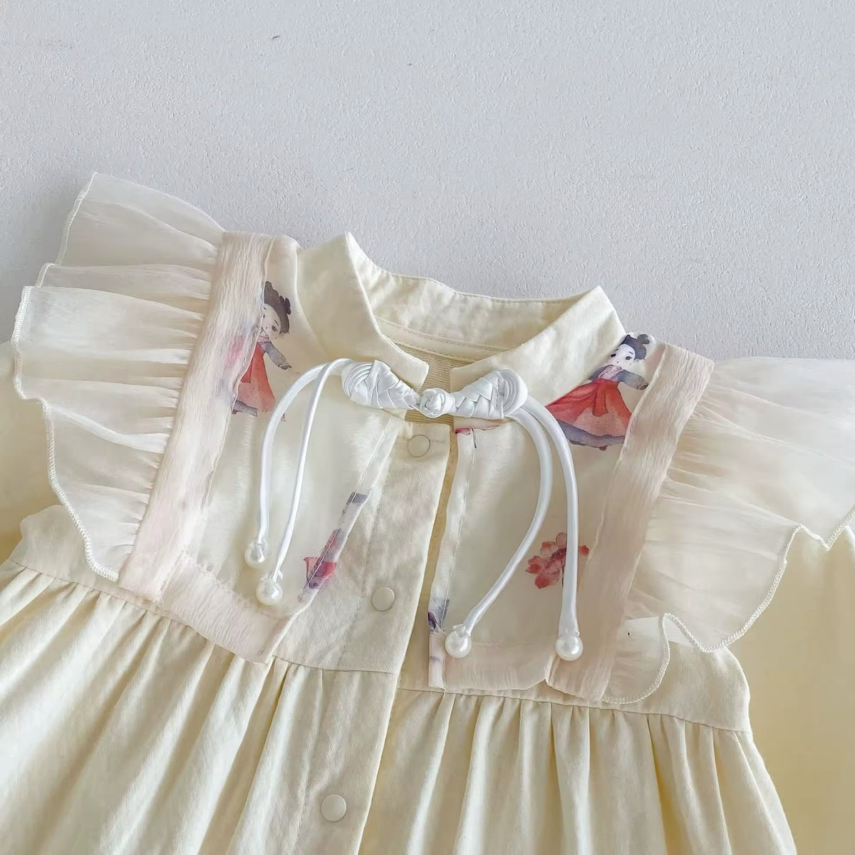 Close-up of floral embroidery and tie neck on cream baby jumpsuit