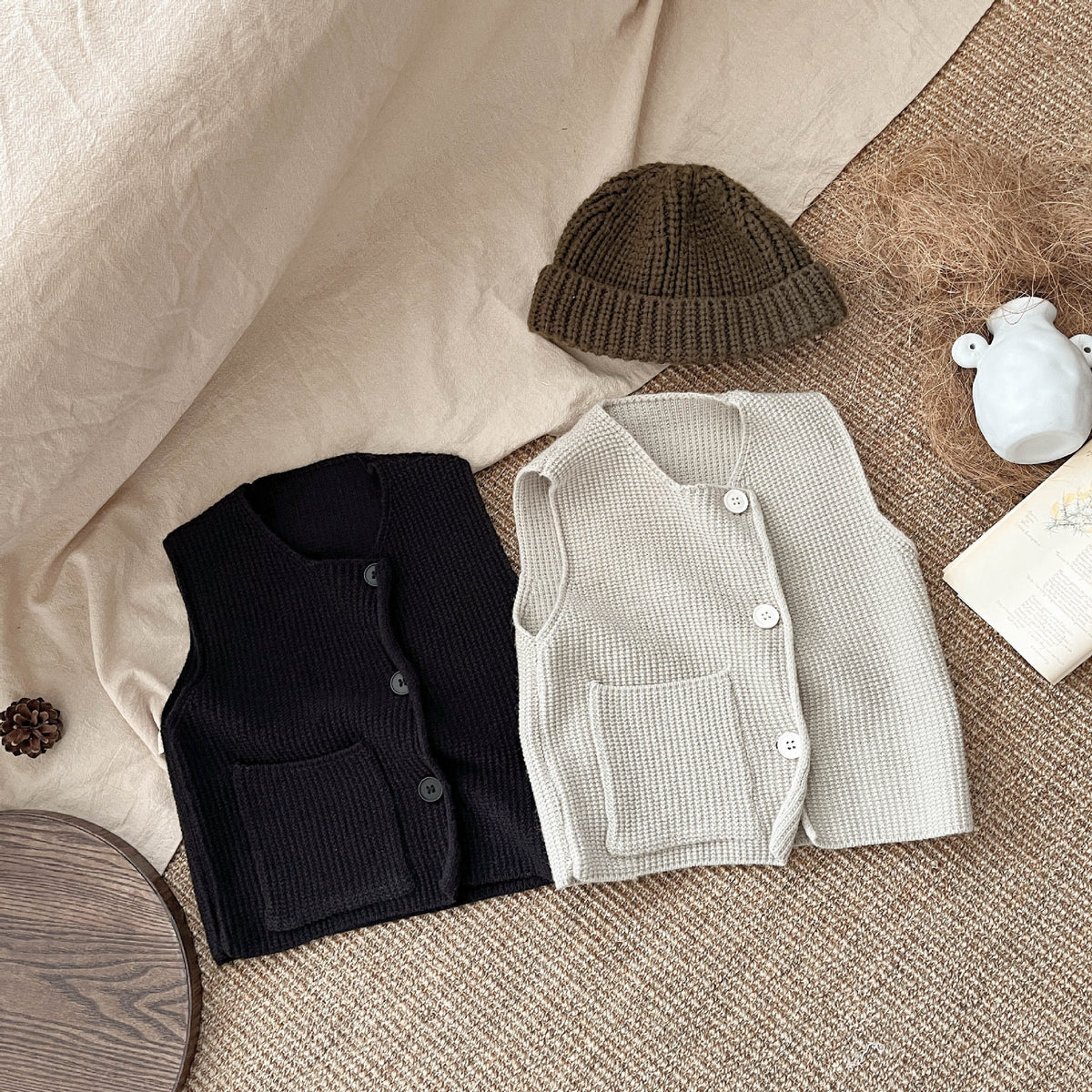 Black and beige knit vests laid flat with beanie