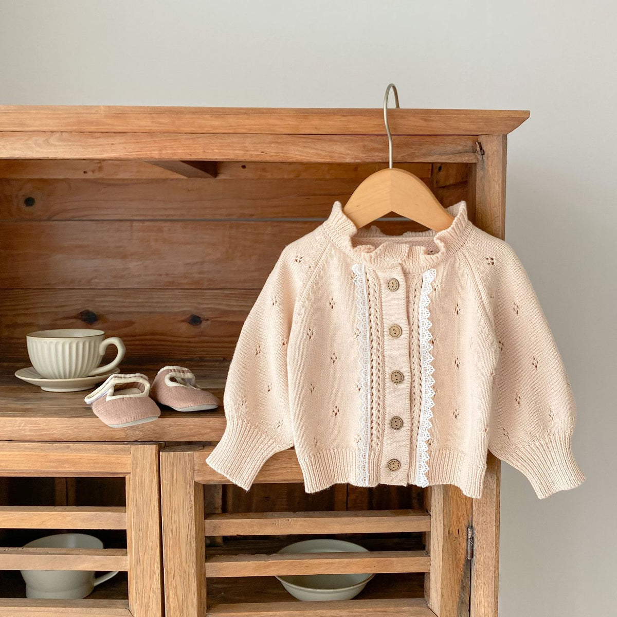 Cream pointelle knit baby cardigan with lace trim and ruffle collar on a wooden hanger