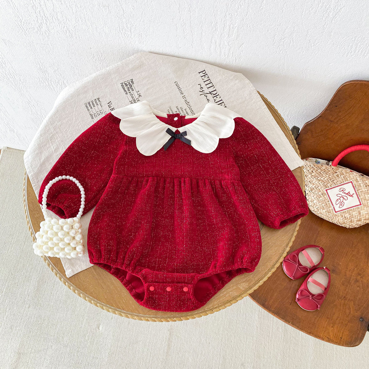 Red textured baby romper with petal collar on a round table