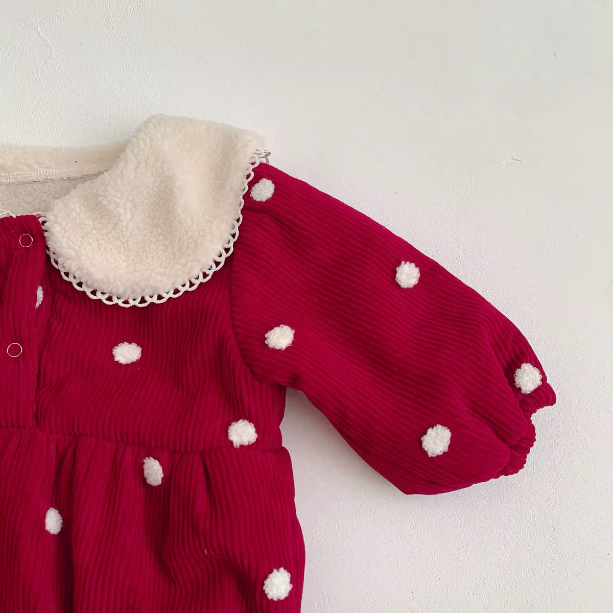 Close-up of puff sleeve and pom-pom dots on red corduroy baby romper