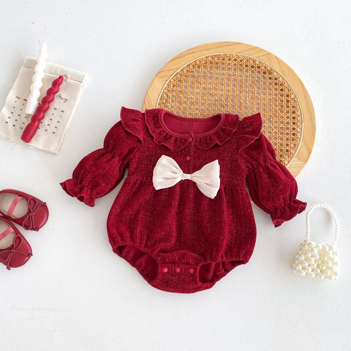 Red ruffle baby romper with cream bow laid flat with shoes