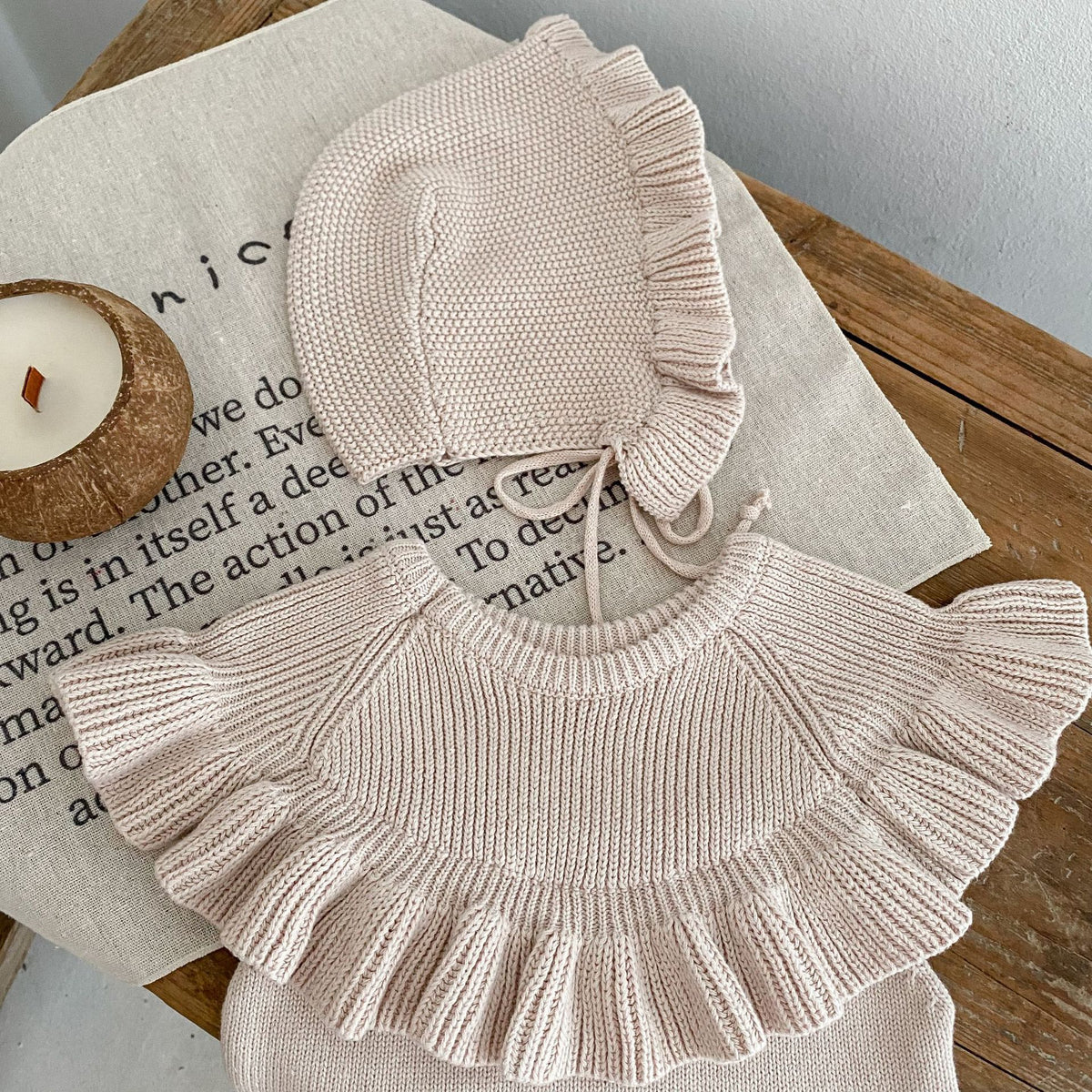 Knit ruffle romper and frilled bonnet laid flat on a table