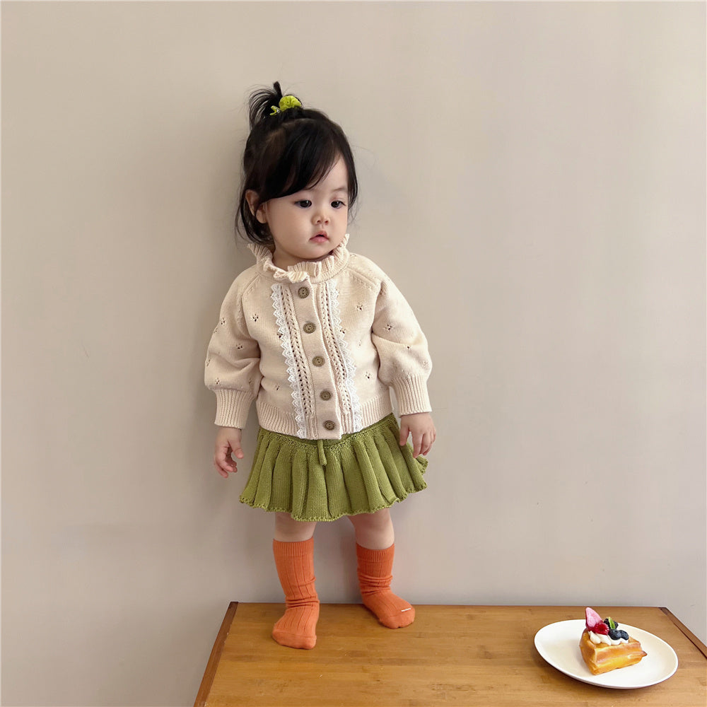 Toddler girl wearing cream lace trim knit cardigan with green pleated skirt