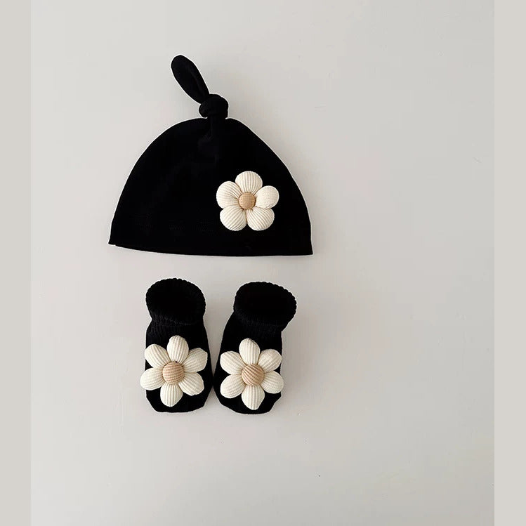 Black knot baby beanie and socks with cream daisy flowers, flat lay