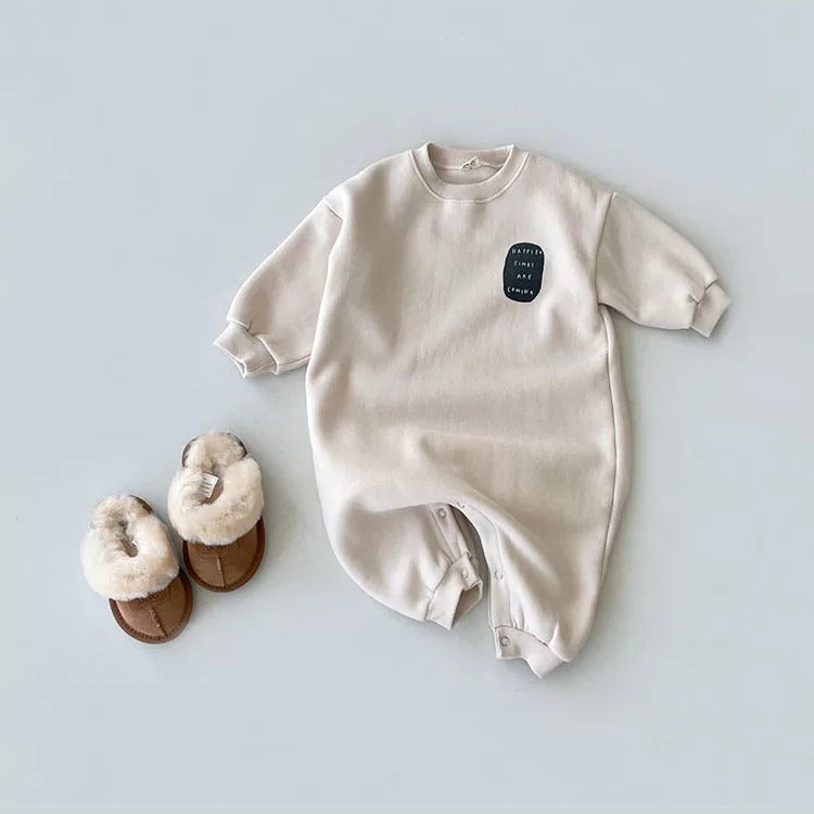 Oat beige sweatshirt baby romper with a "Happier times are coming" patch, flat lay