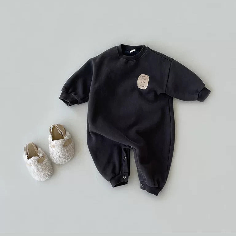 Charcoal sweatshirt baby romper with a cream slogan patch, flat lay