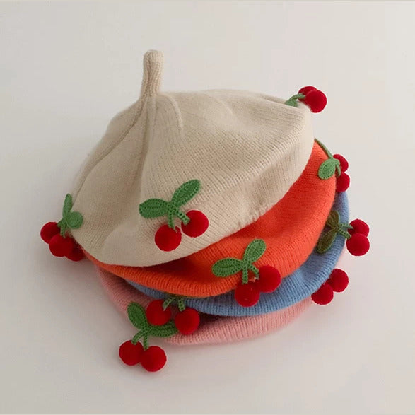 Stack of knit cherry berets for babies in cream, tangerine, sky blue and blush