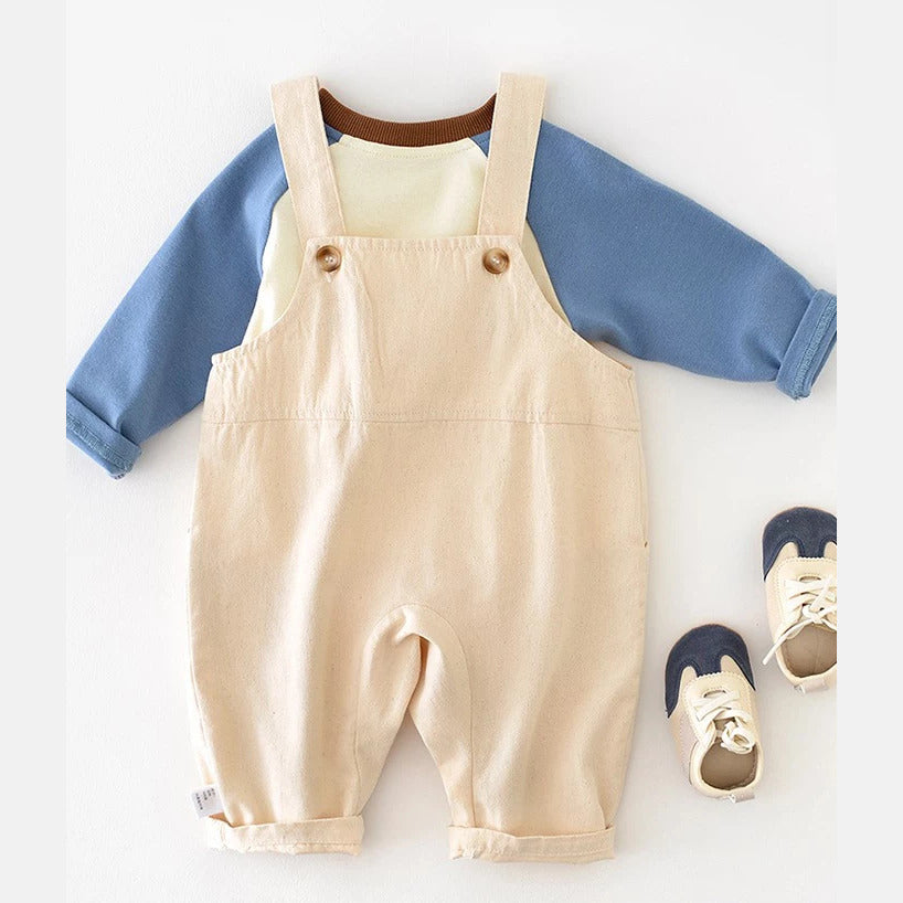 Back view of beige baby overalls with wooden-look buttons over a blue raglan tee