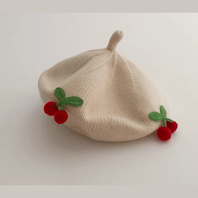 Close-up of a cream knit baby beret with crochet cherries