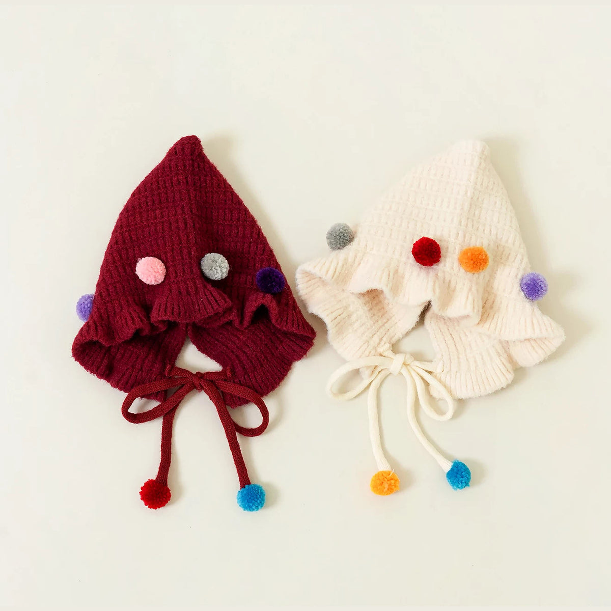Berry and cream ruffled pixie bonnets laid flat with pom-pom ties