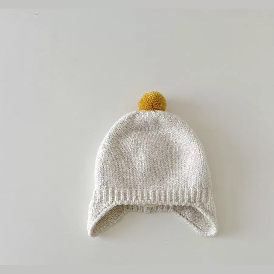 Oatmeal knit baby earflap hat with mustard pom-pom, flat lay