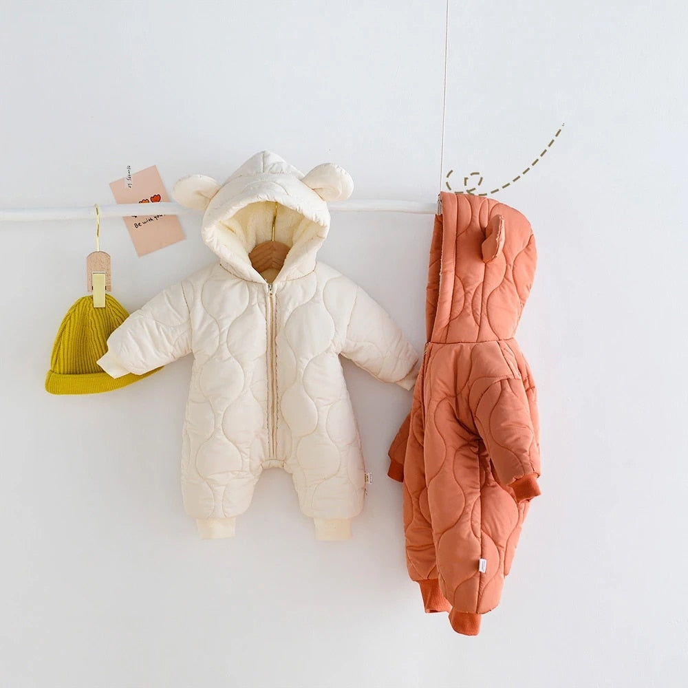 Adorable quilted baby jumpsuits in cream and burnt orange, featuring cozy hooded designs with soft bear ears. The padded, full-length suits have a zipper front for easy wear, and ribbed cuffs for added warmth. Perfect for keeping little ones snug and stylish in cold weather.