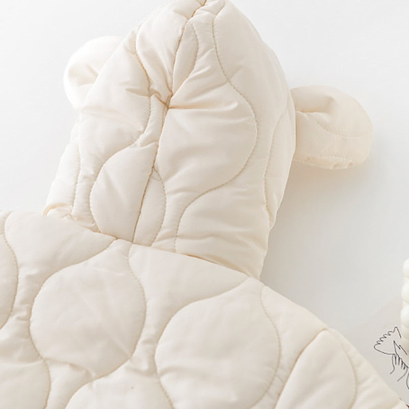 Close-up of the hood on a cream-colored quilted baby jumpsuit, featuring adorable bear ears. The quilted texture adds a soft, padded look, providing warmth and a charming, playful detail that’s perfect for babies in cooler weather.