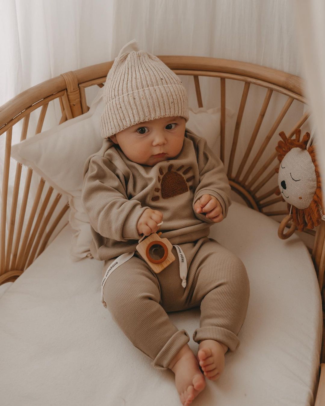 Baby in khaki sun tracksuit set sitting in a rattan crib