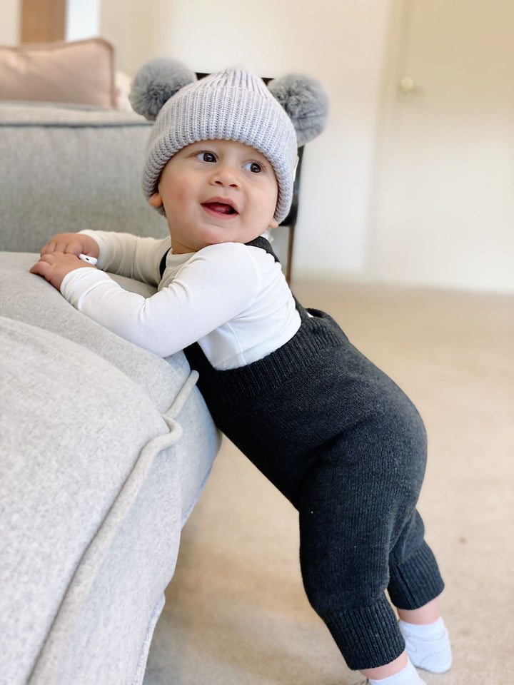 Baby wearing dark gray knitted overalls and white top
