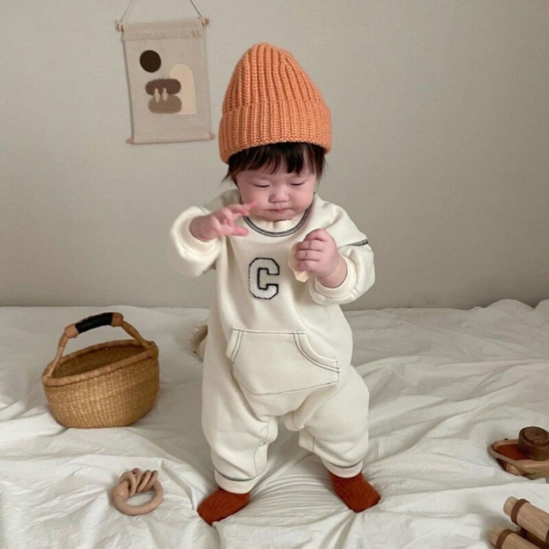 Baby standing in white C letter jumpsuit and beanie