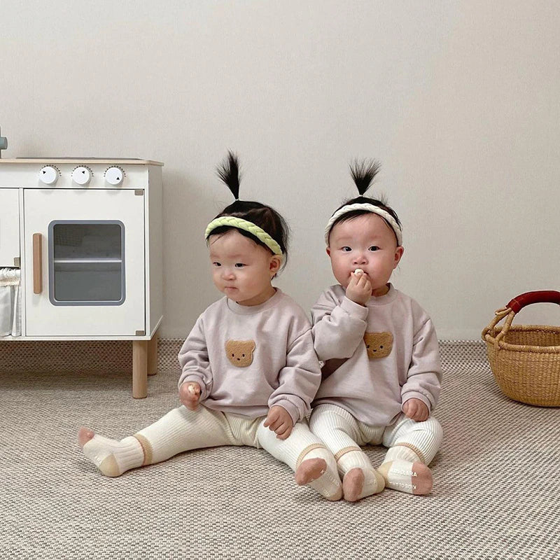 Two babies wearing bear patch sweatshirts