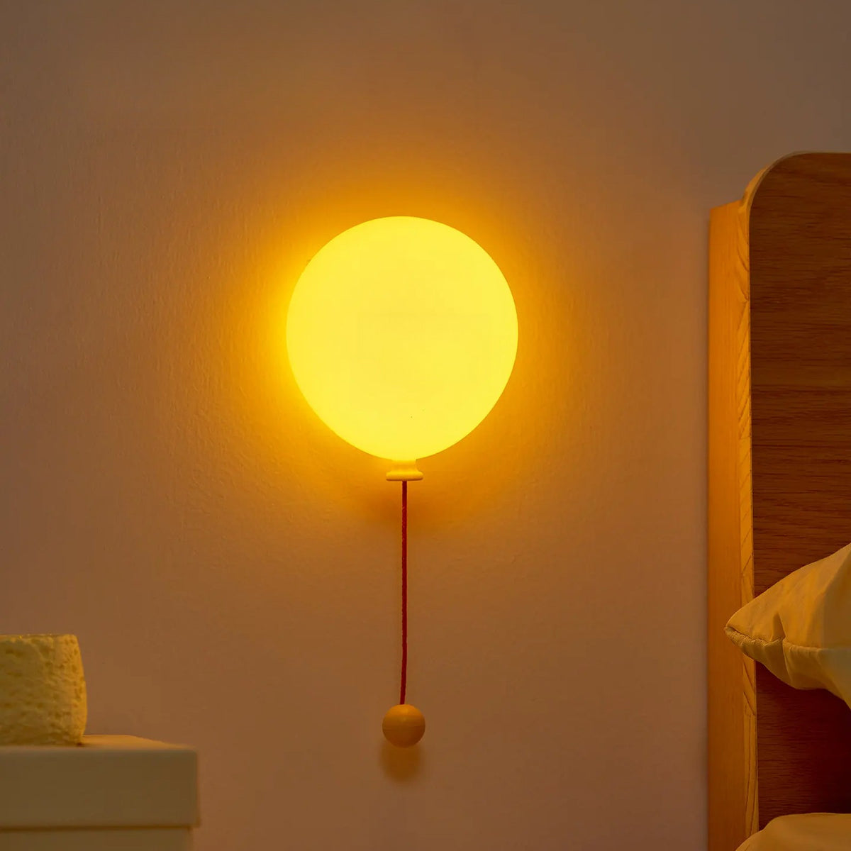 Glowing yellow balloon night light on a bedroom wall with a red pull cord