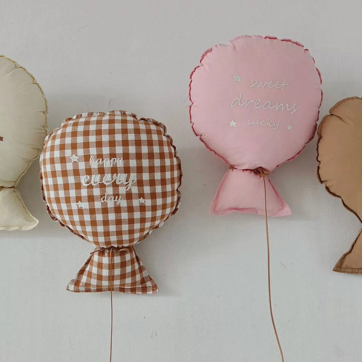 Gingham and pink balloon pillows hanging on a wall with their strings