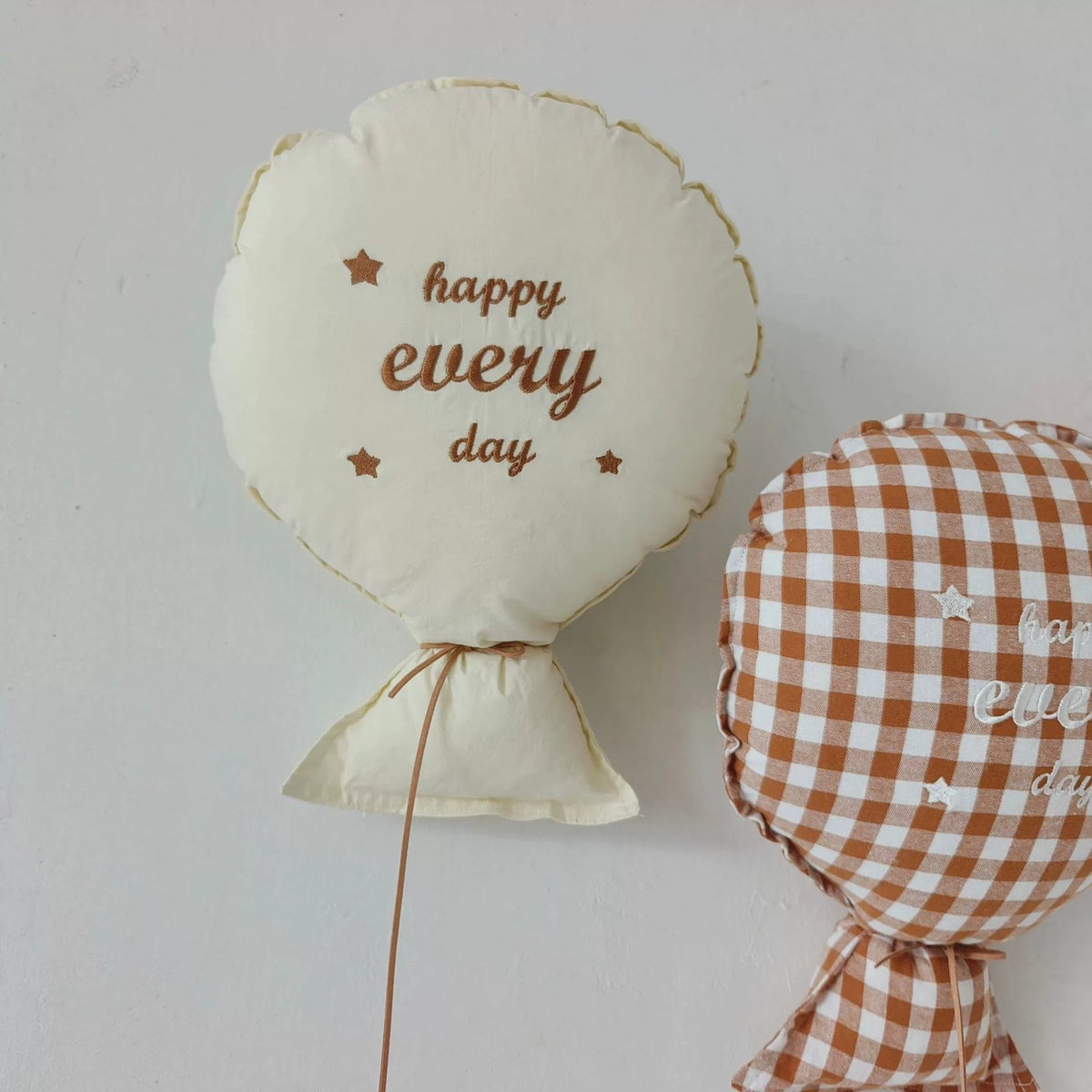 Cream balloon pillow embroidered "happy every day" hanging on a wall