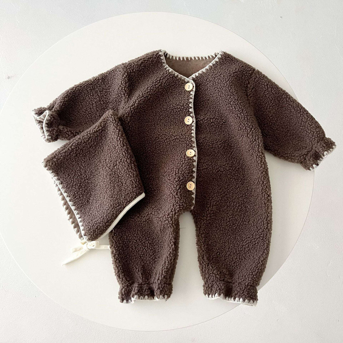 Cocoa sherpa baby romper laid flat on a round backdrop