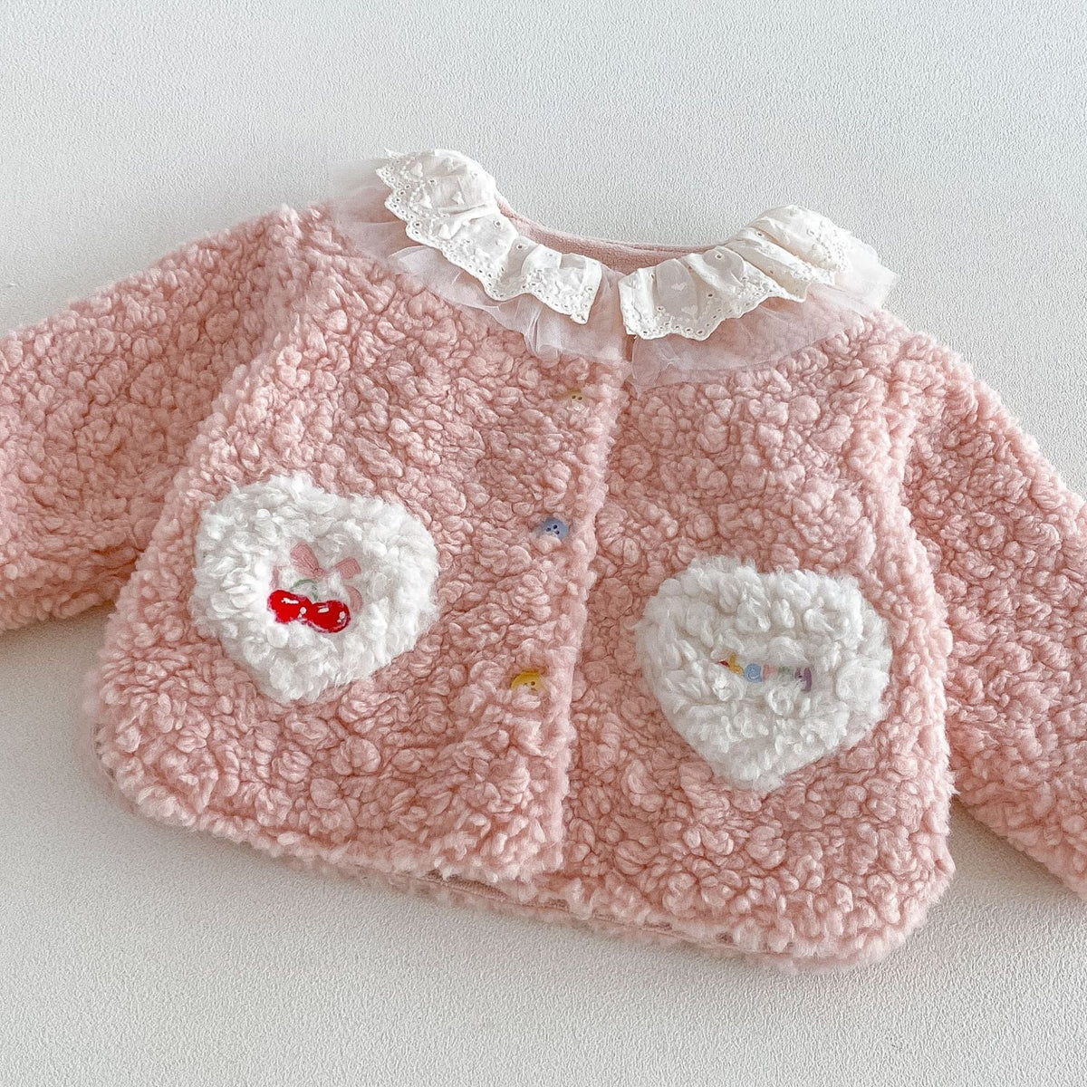 Close-up of the cherry embroidered heart pocket on the pink sherpa jacket