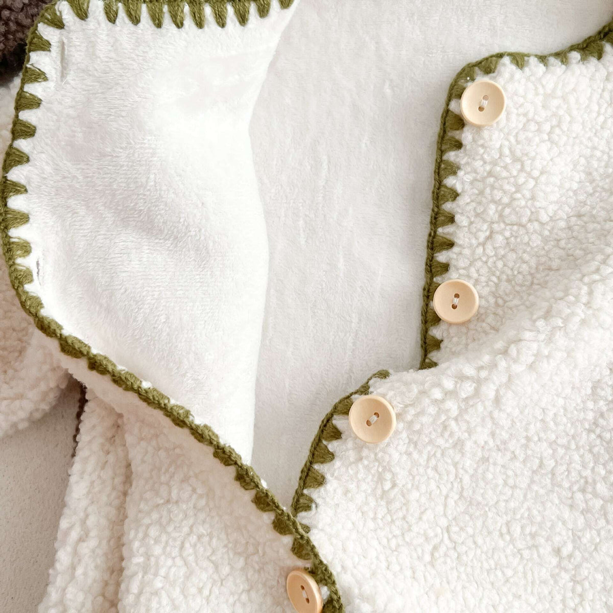 Close-up of the stitched neckline and buttons on the ivory sherpa romper