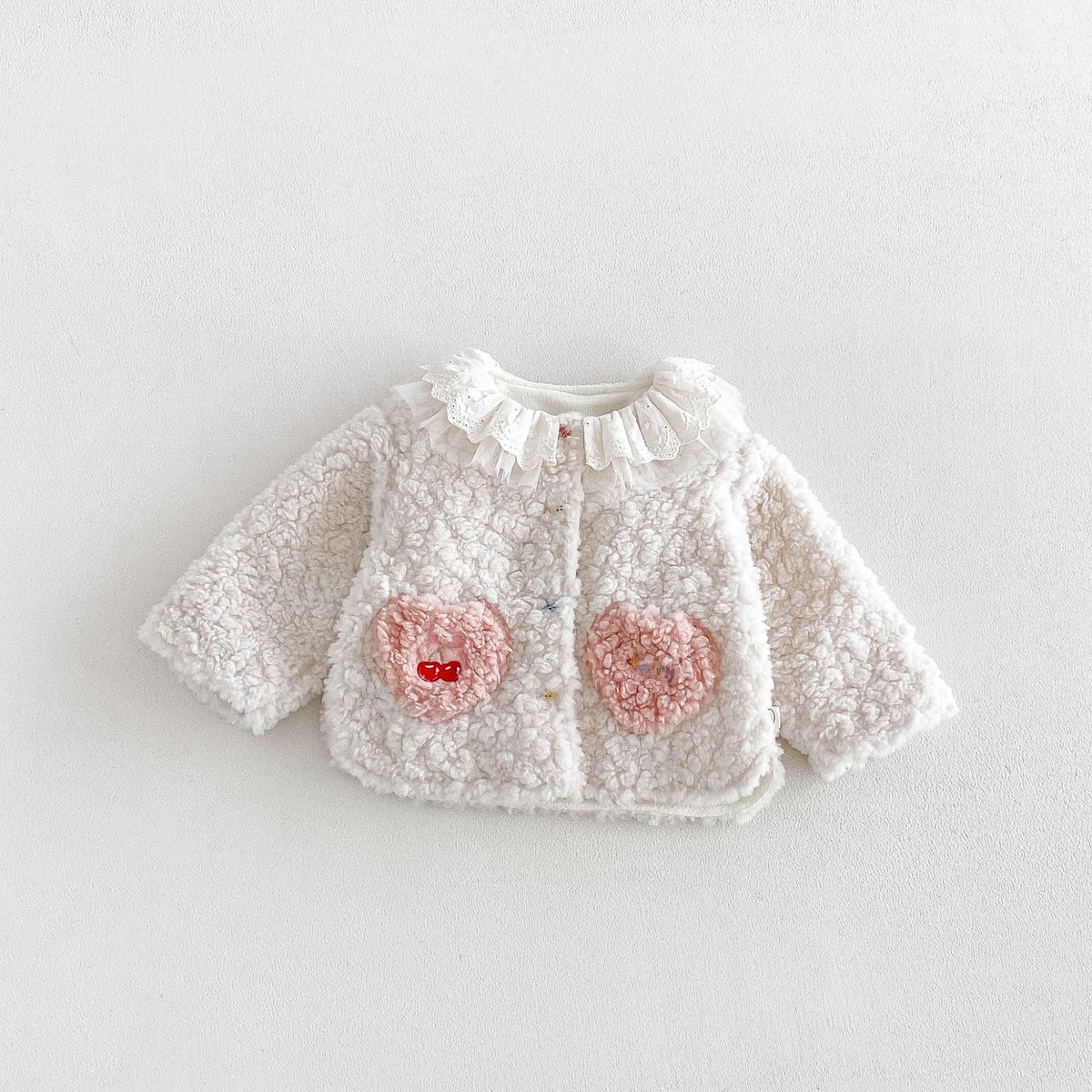 Ivory sherpa jacket with ruffle collar and pink heart pockets, flat lay