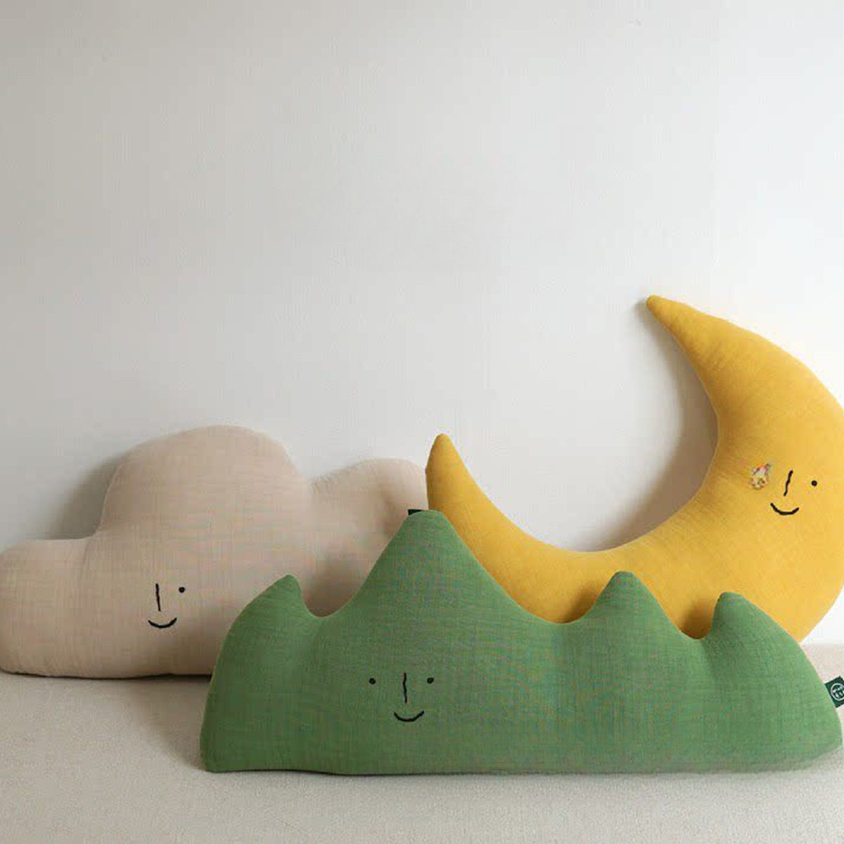 Cloud, mountain and moon muslin cushions on a nursery bed