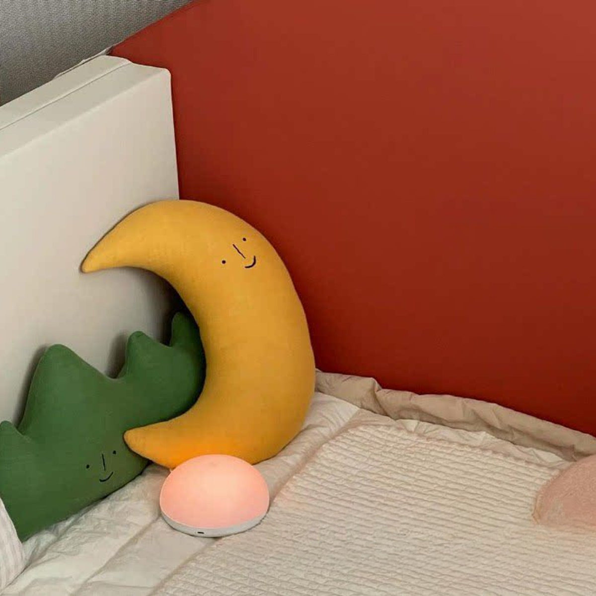 Yellow moon and mountain cushions on a kids bed with a night light