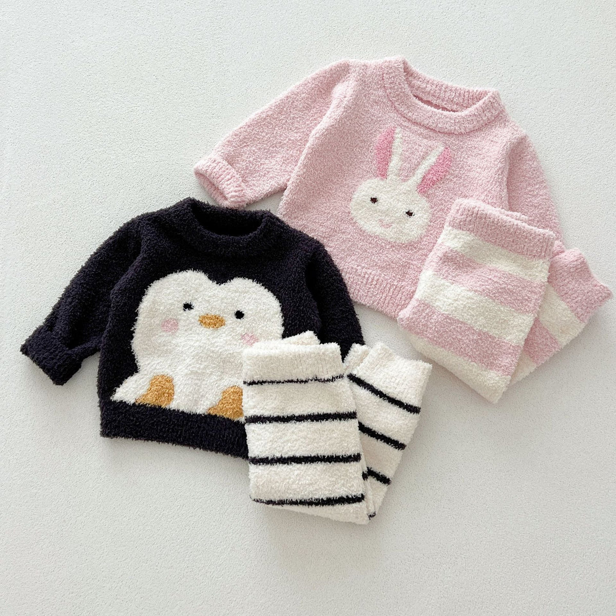 Penguin and bunny fuzzy knit sweaters with striped knit pants, flat lay