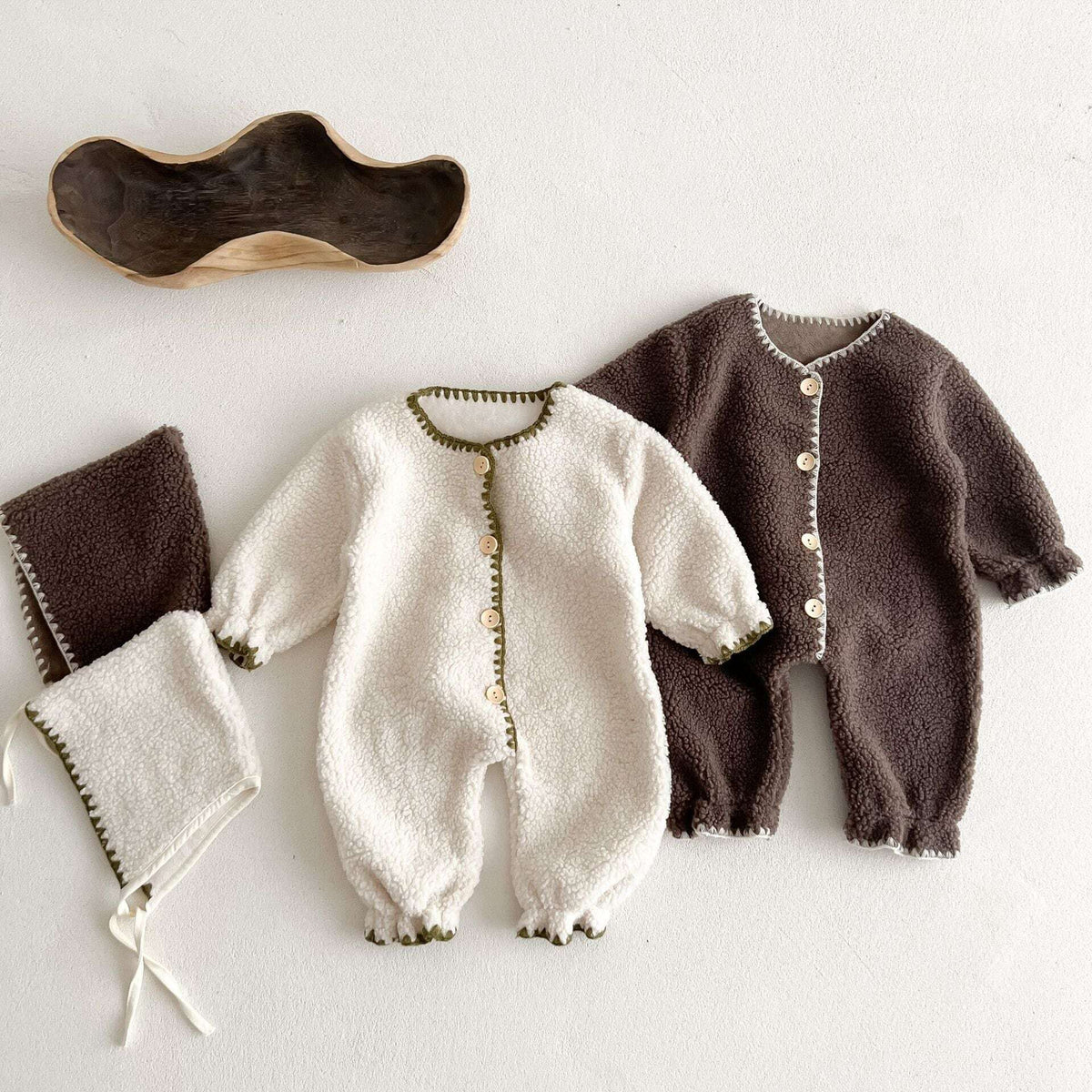 Ivory and cocoa sherpa baby rompers with matching bonnets, flat lay