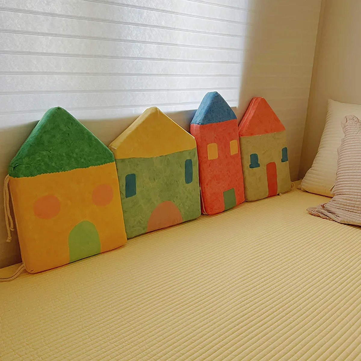 Fairytale Village house-shaped cushions set in green, mustard, red and blue on a bed
