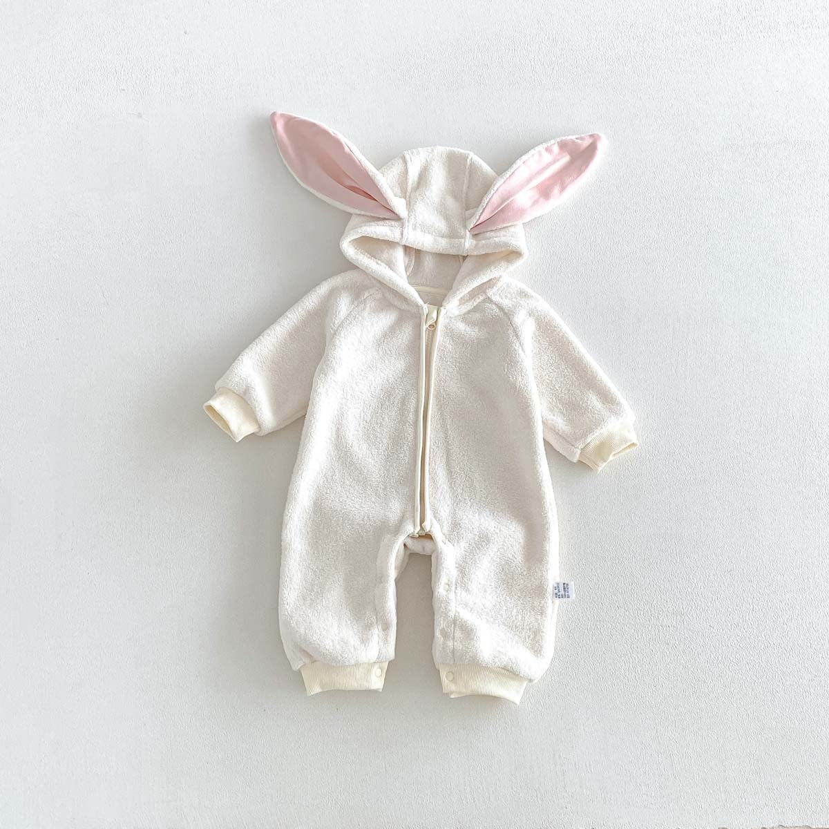 Ivory fleece baby romper with pink-lined bunny ears, flat lay